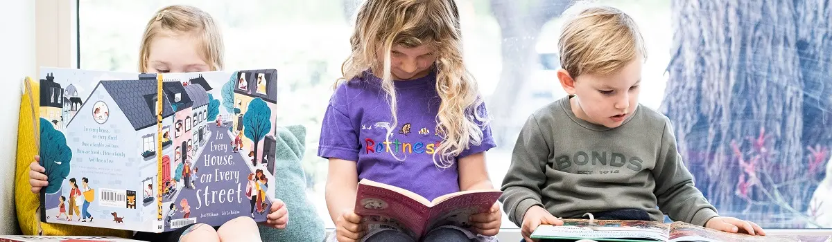 Three children in the library sitting down, each reading a book.